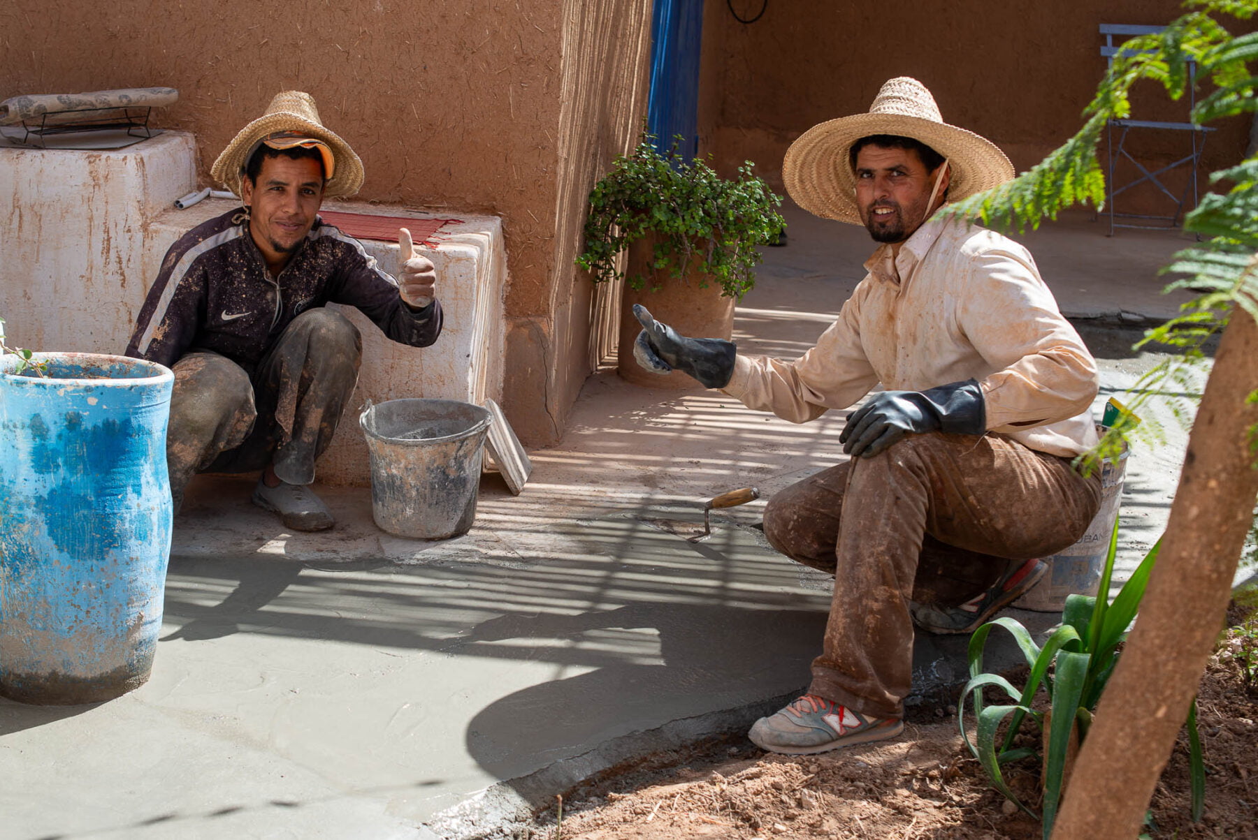 two men wearing straw hats and sitting on a sidewalk
